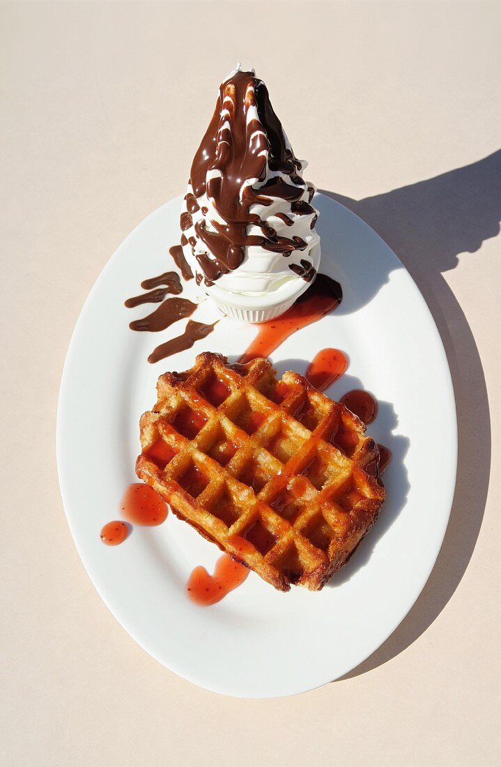 A Belgian waffle with strawberry sauce and soft ice with chocolate glaze