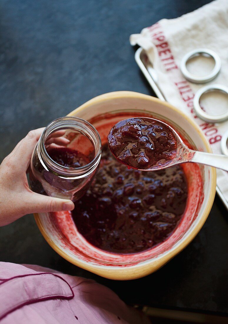 A woman transferring strawberry jam into a jar