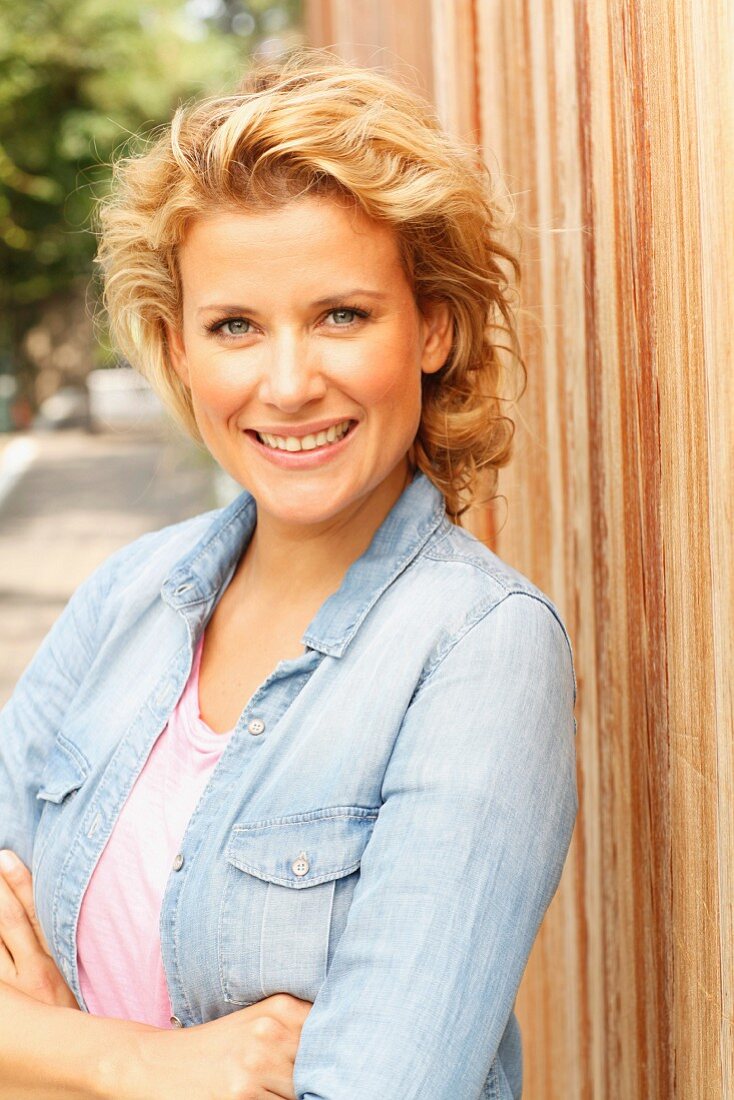 A blonde woman wearing a denim shirt leaning on a fence