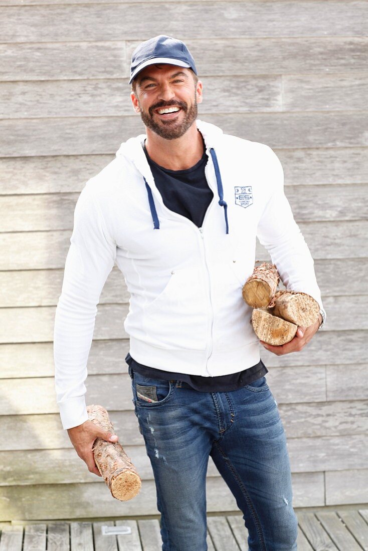 A man wearing sports clothes standing against a fence holding wood