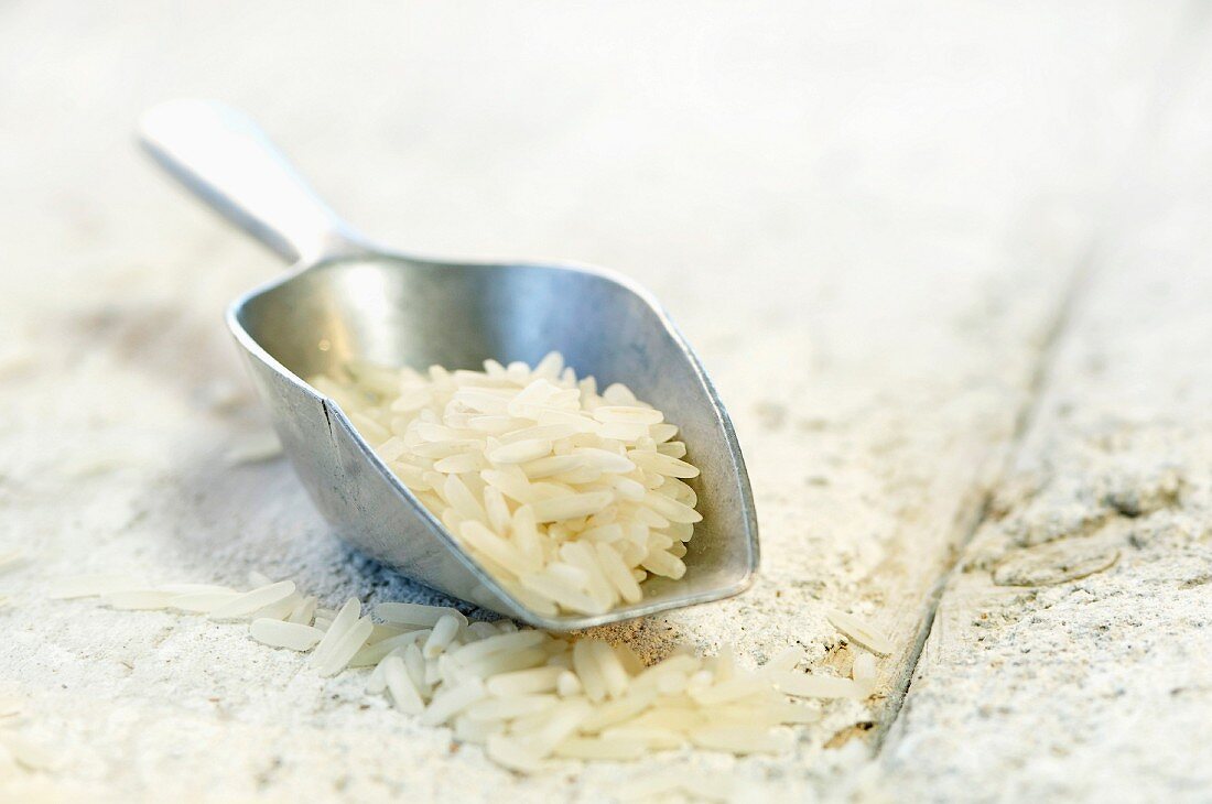 Rice on a metal scoop and on a wooden surface