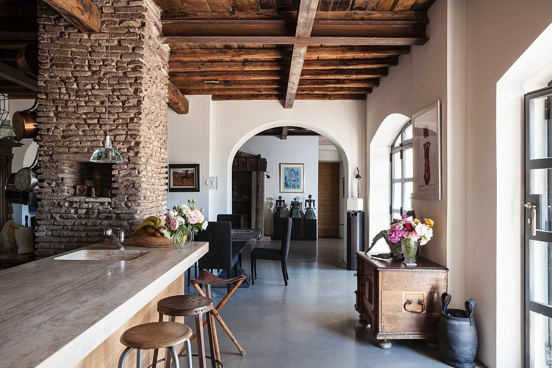 Blick von Küchentheke in offenen Wohnbereich mit Rundbogendurchgang in renoviertem Landhaus mit rustikaler Holzbalkendecke