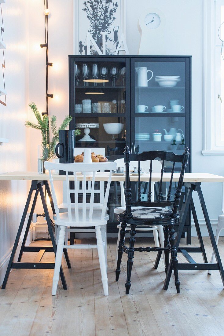 Dining table and various black and white chairs in front of crockery in display case
