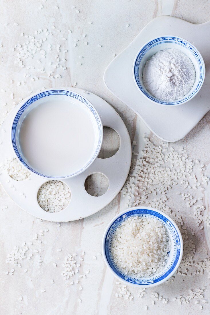Reisdrink, Reismehl und Reiskörner in Schalen auf Marmorfläche (Draufsicht)