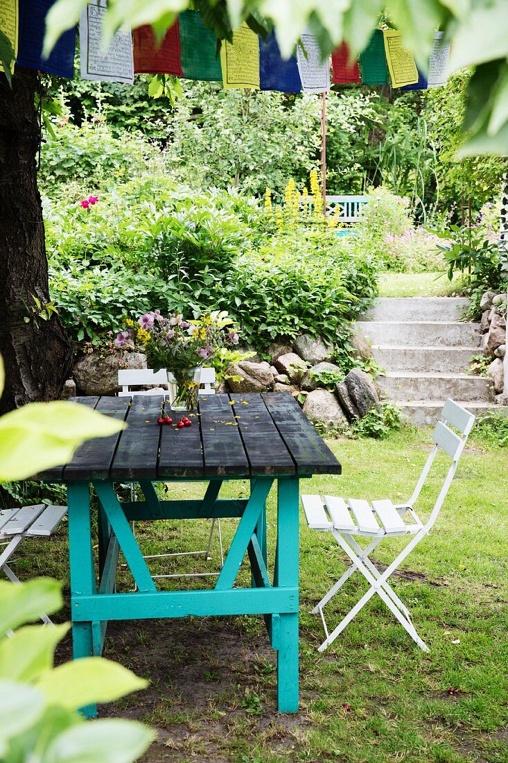 Rustikaler Gartentisch mit türkis lackiertem Untergestell und Klappstühle, im Hintergrund Treppenaufgang im Garten