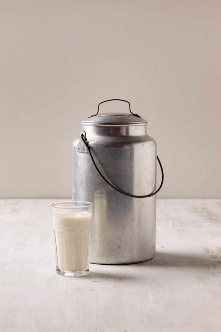 Ein Glas veganer Milchersatz vor Milchkanne aus Metall
