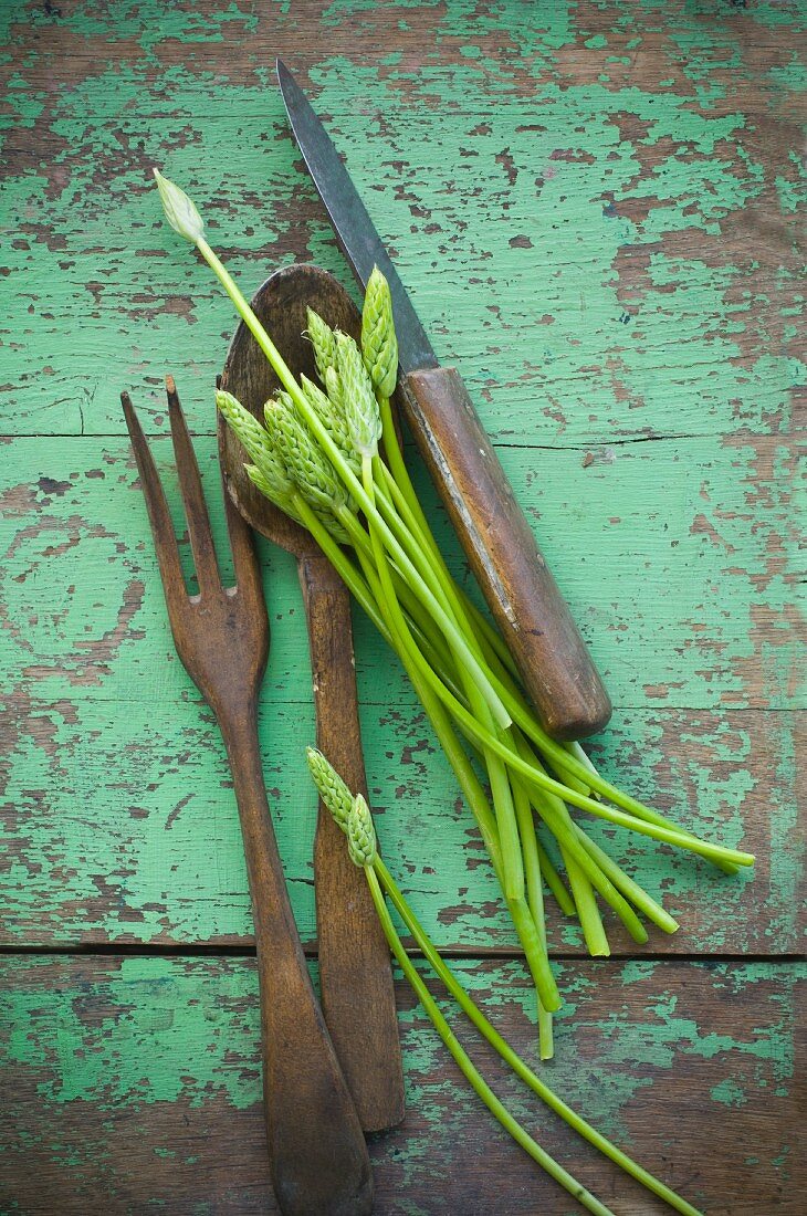 Wild asparagus on a rustic wooden table with salad servers and a knife