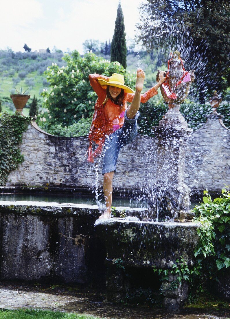 A young woman by a fountain wearing a transparent shirt and jeans