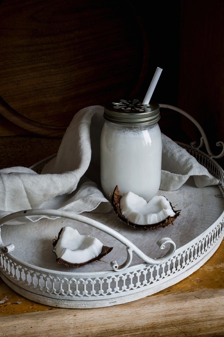 Vegane Kokosmilch in Schraubglas mit Strohhalm auf Tablett