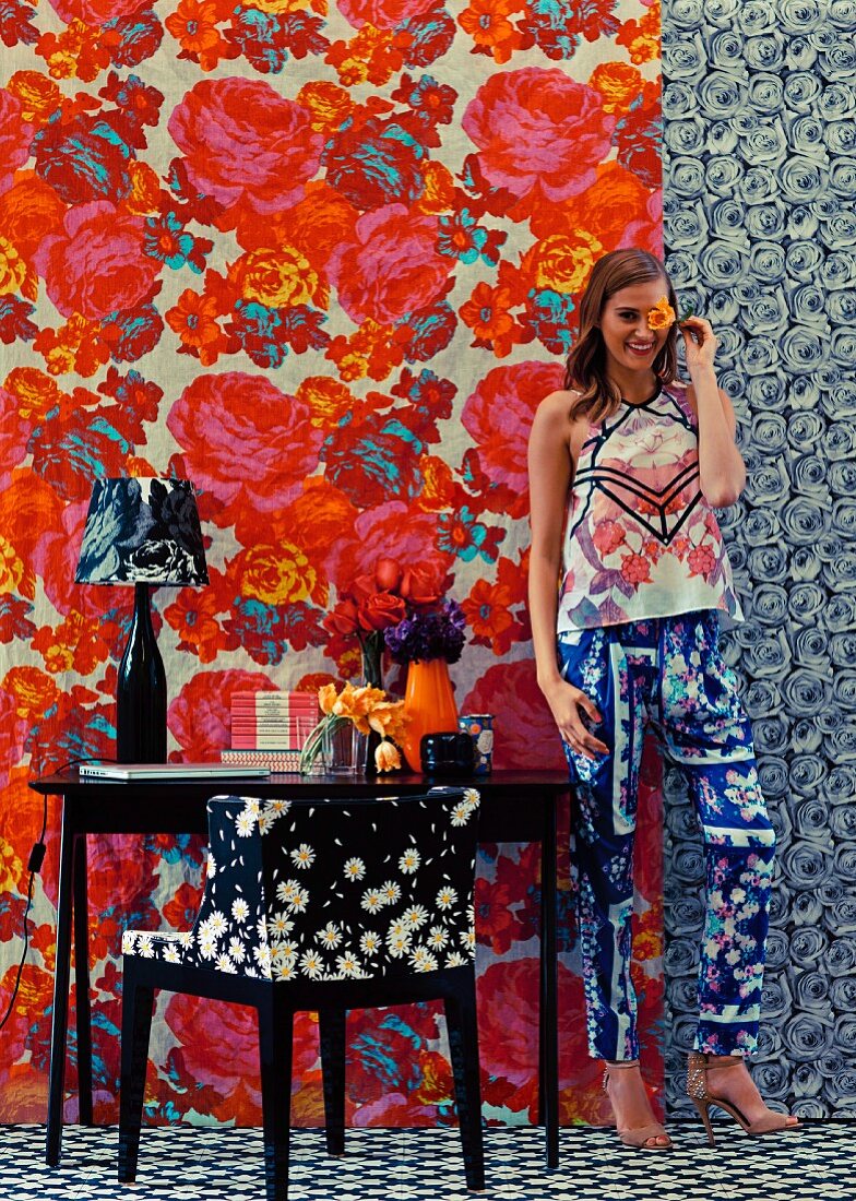 Junge Frau in Zimmer mit verschiedenen Mustern an Tapete, Teppich, Sessel und Kleidung