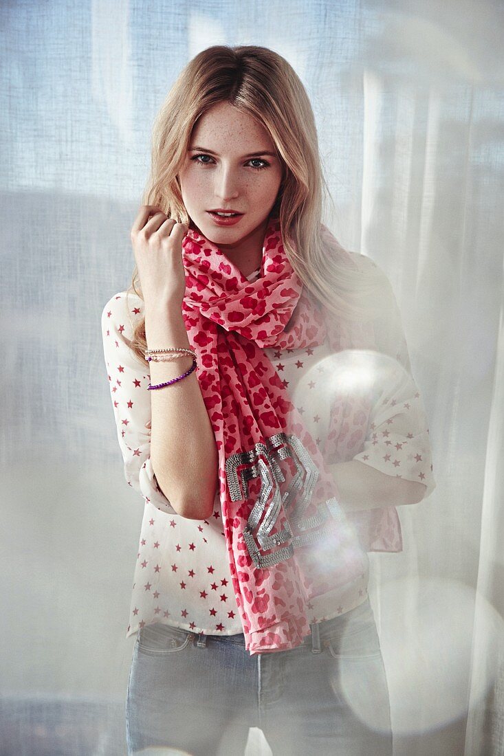 A young woman wearing a long-sleeved short and a pink, cow-patterned scarf