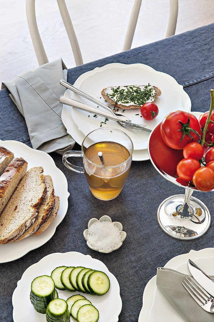 Gedeckter Tisch zum Abendessen mit Schnittlauchbrot, Tomaten und Kräutertee