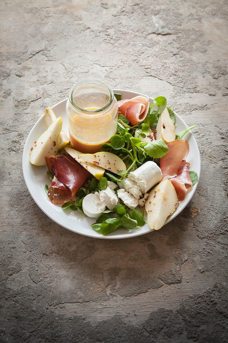 Salad with a roll of goats cheese roll, pears, Parma ham and pine nuts