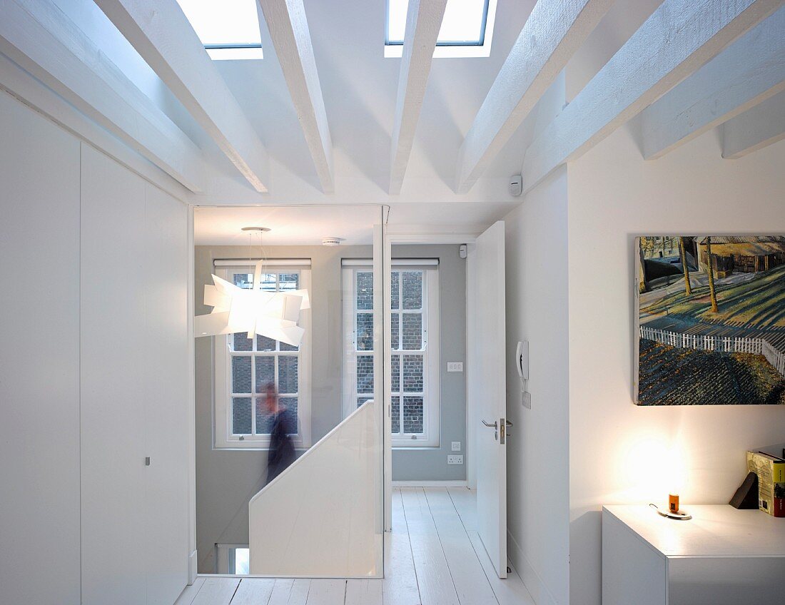Bright, attic hallway with white, wooden beams below skylights and open door leading to stairwell