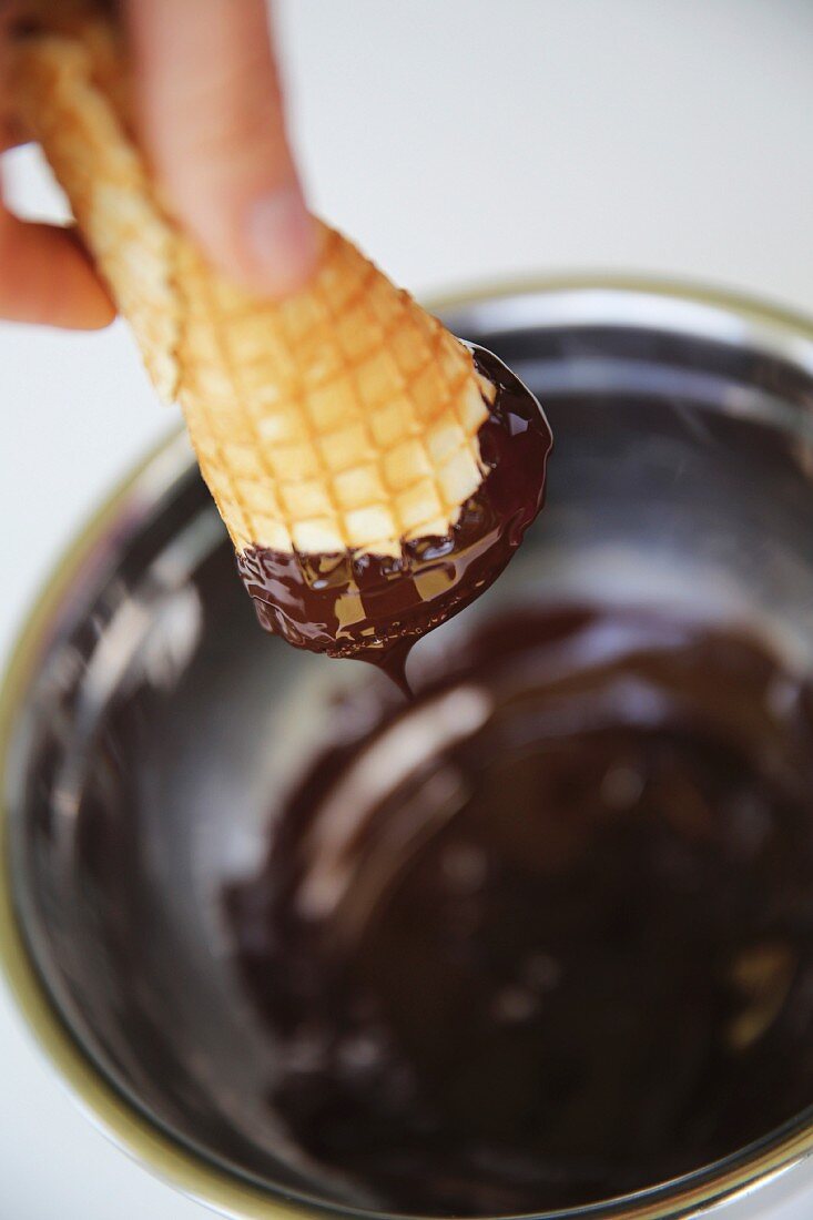 An ice cream cone being dipped into melted chocolate