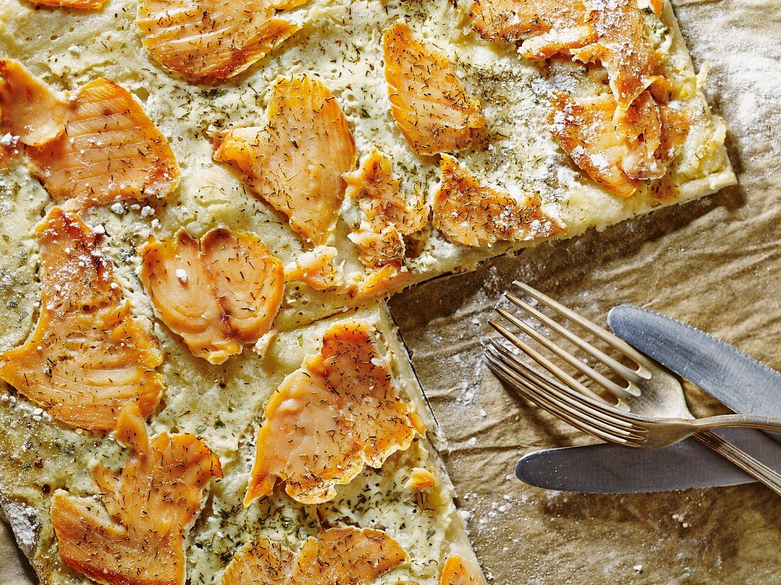 Ofenfrischer Flammkuchen mit Lachs, angeschnitten auf dem Backblech