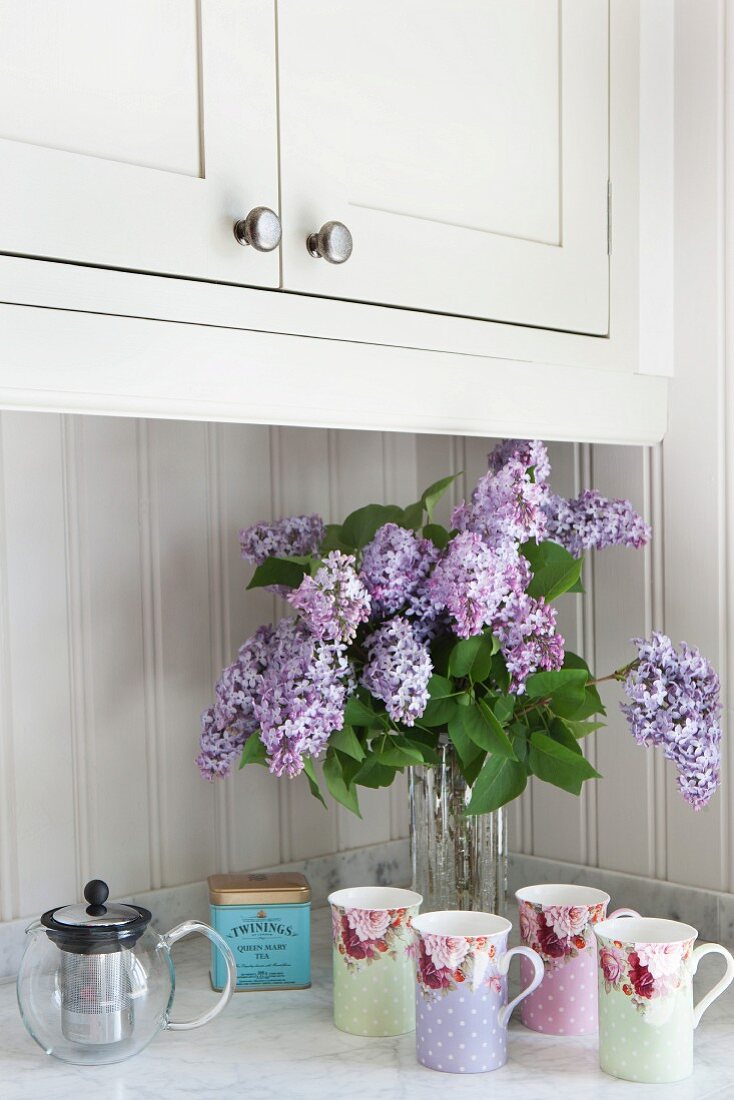 Vintage-style beakers and vase of lilac on kitchen counter with Carrara marble worksurface
