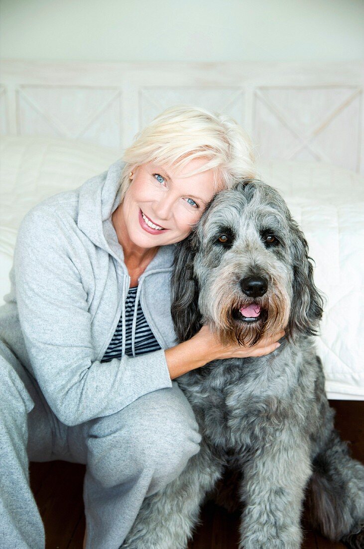 A blonde woman and a dog in front of a white bed