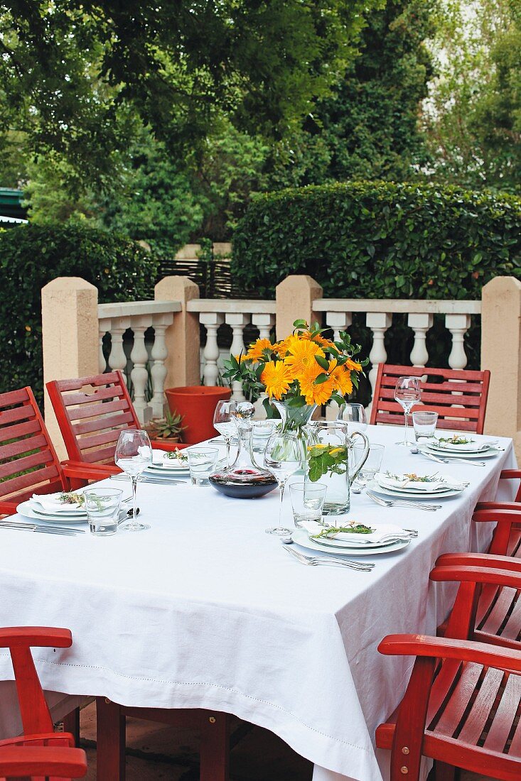 A table laid on a terrace with a white cloth, a bunch of orange flowers and carafes of water and wine