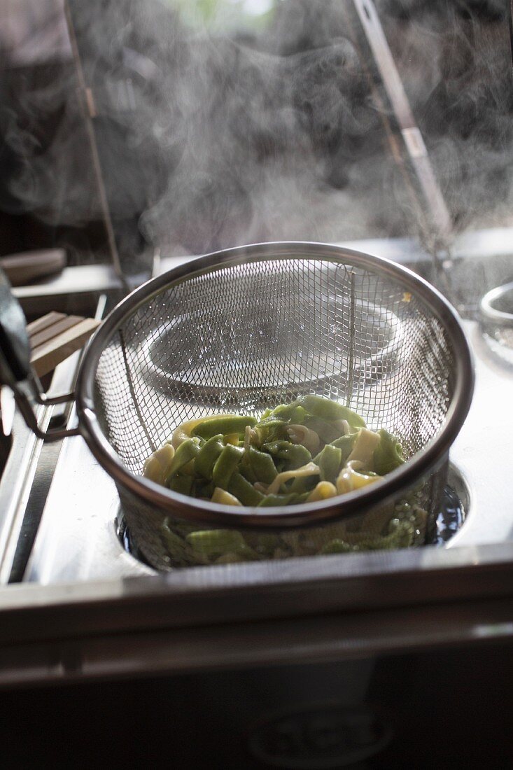 Green and white tagliatelle being steamed in a sieve