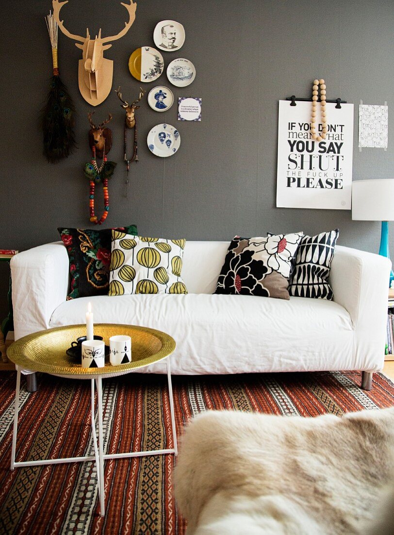 Tray table, white sofa with patterned scatter cushions on rug below decorations on grey wall