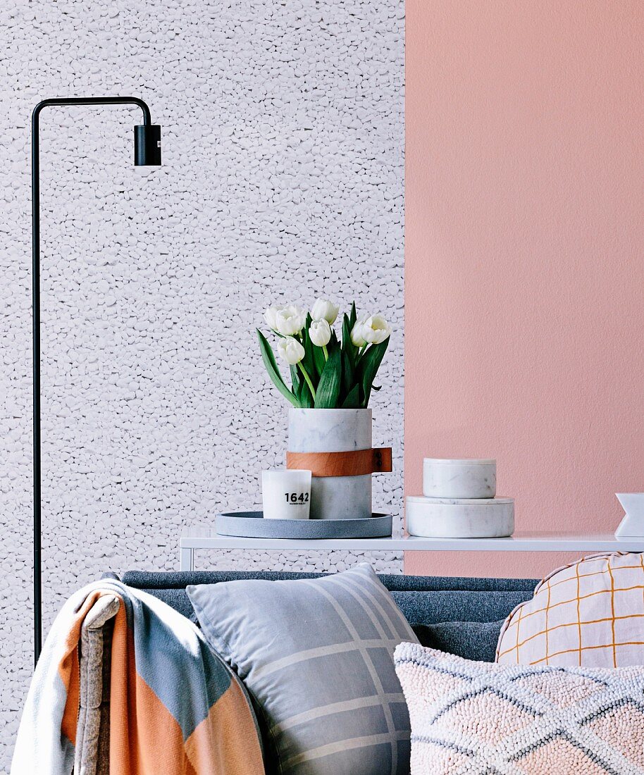 Cushions on sofa in front of console table with marble bowls and vase with white bouquet of tulips