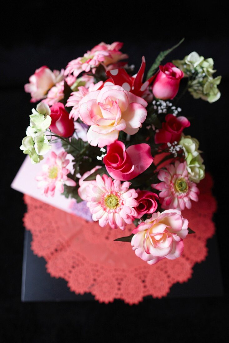 Bouquet of roses and gerbera daisies in various shades of red on doily