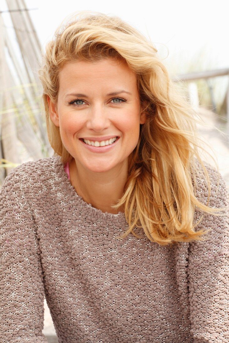 A blonde woman on a beach wearing a taupe jumper