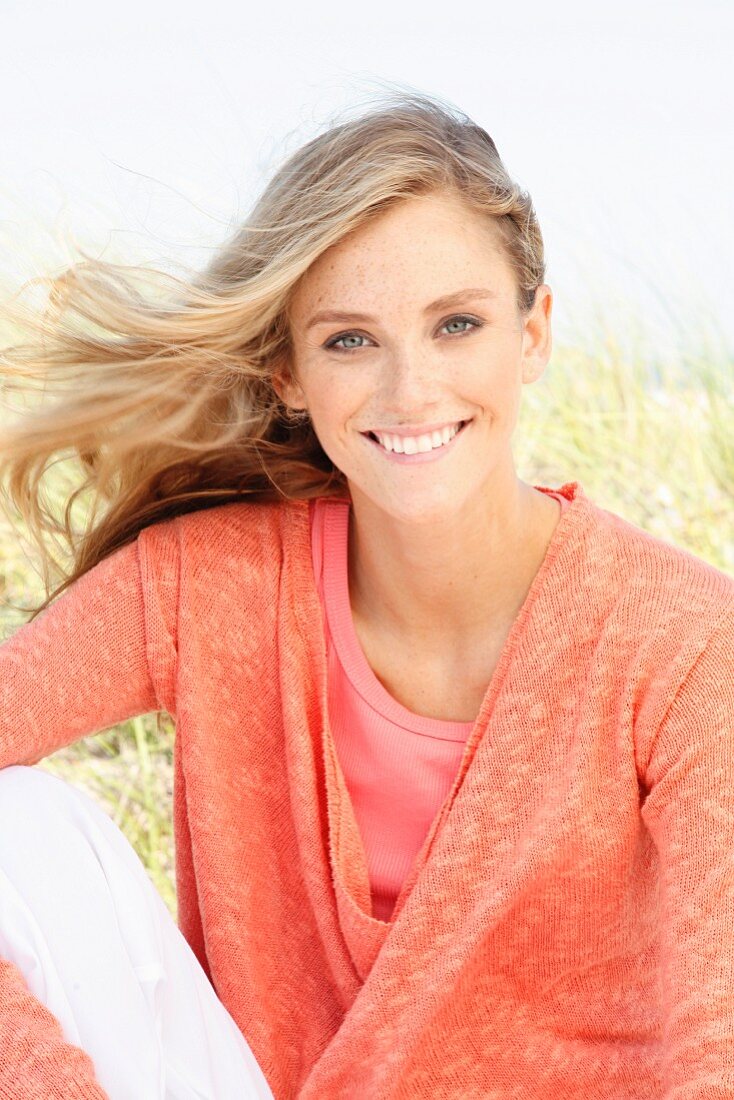 A blonde woman wearing a top and a salmon-pink knitted jumper