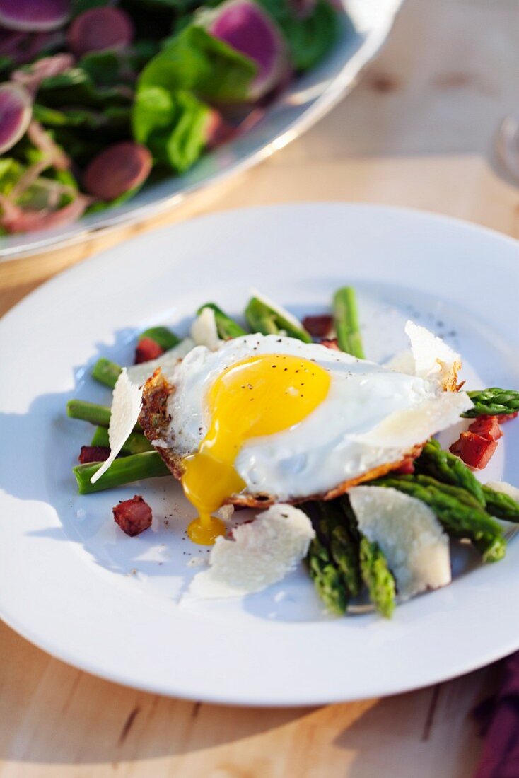 Fried egg on green asparagus with diced bacon and Parmesan cheese