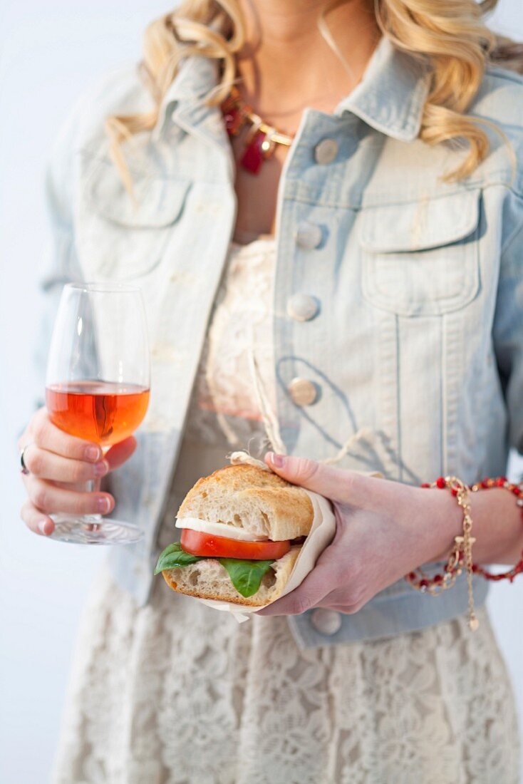 A young woman with a tomato and mozzarella sandwich and an Aperol Spritz