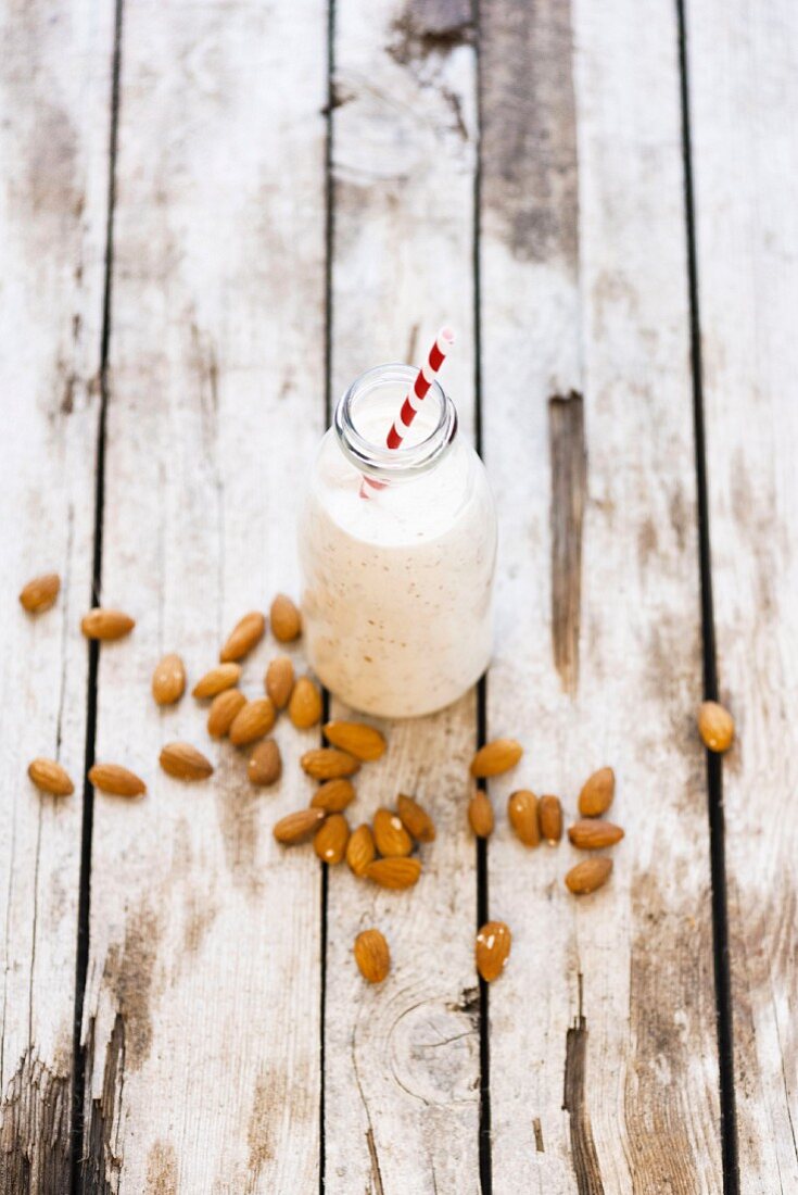 A bottle of almond milk and almond on a wooden surface