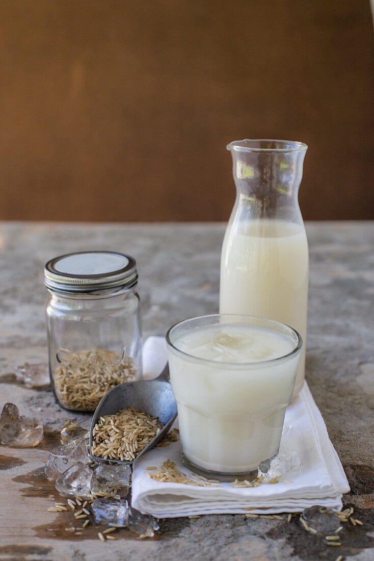 Rice milk in a glass and a jug, ice cubes and brown rice