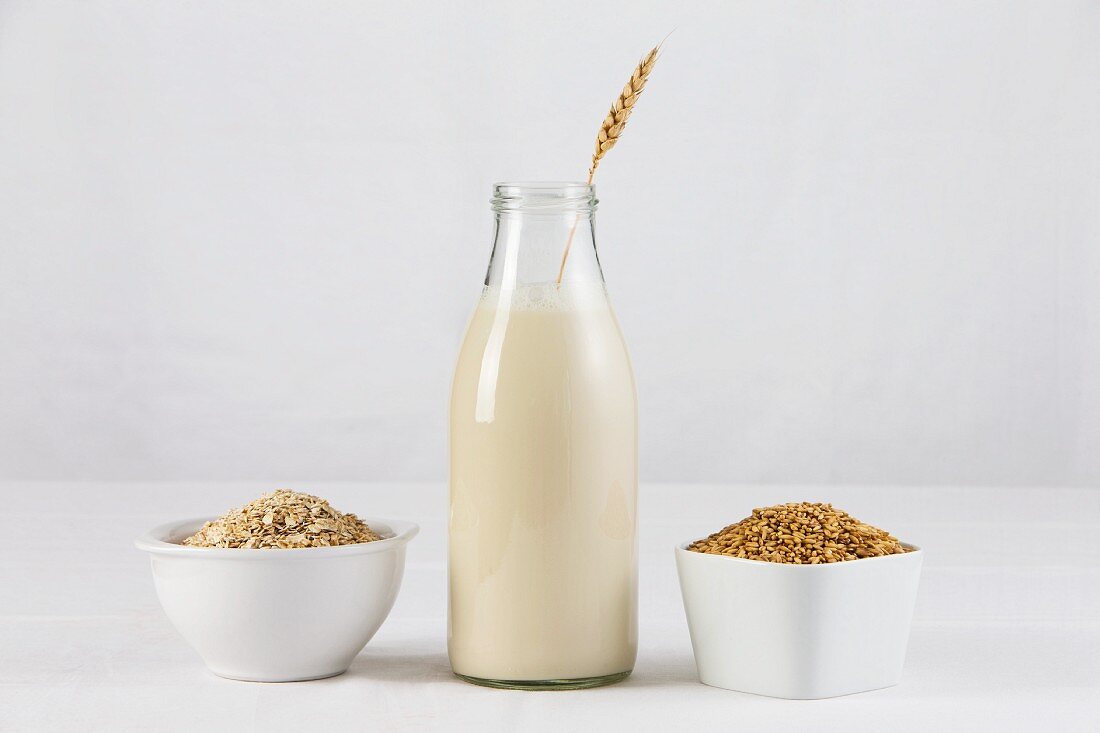 A bottle of oat milk with two dishes of oats and oatmeal