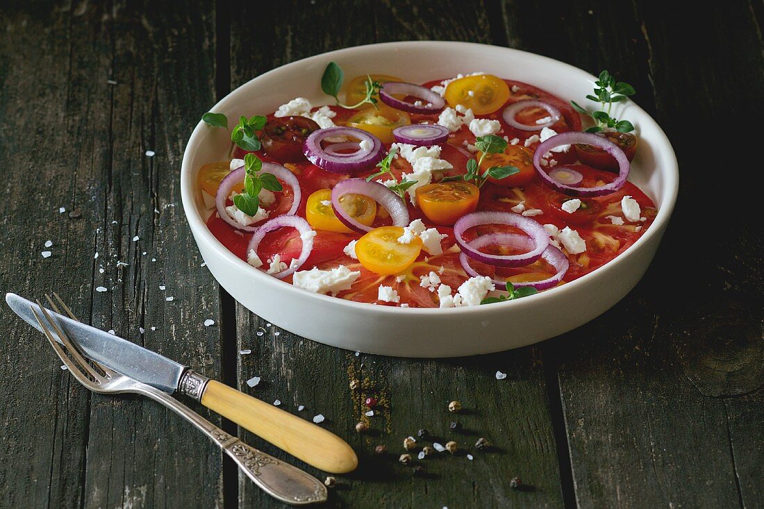 A colourful tomato salad with red onions and feta cheese on an old wooden table