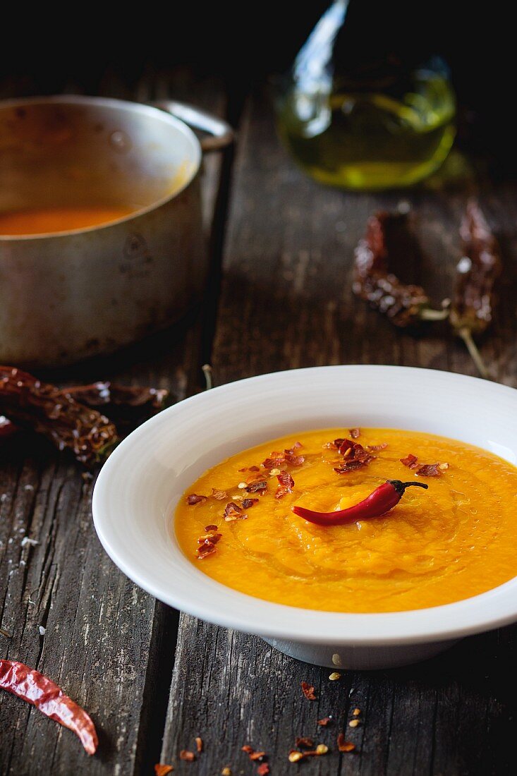 Cream of carrot soup with chilli peppers on a wooden table