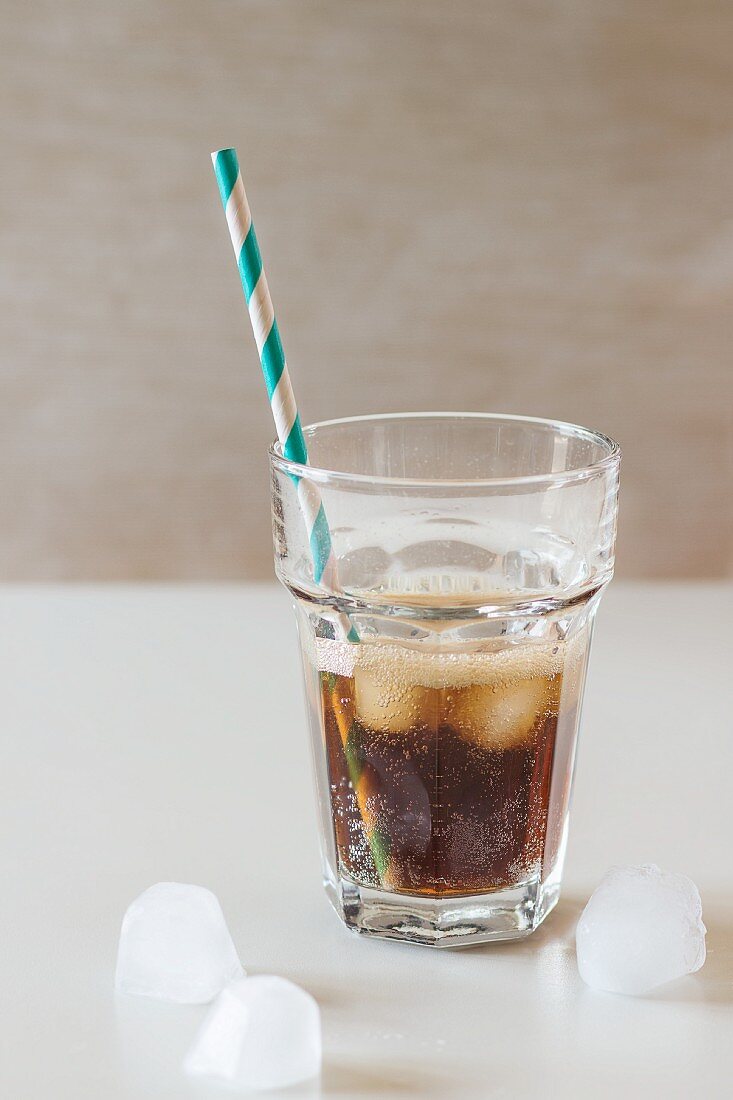 A glass of cola with ice cubes and a retro straw