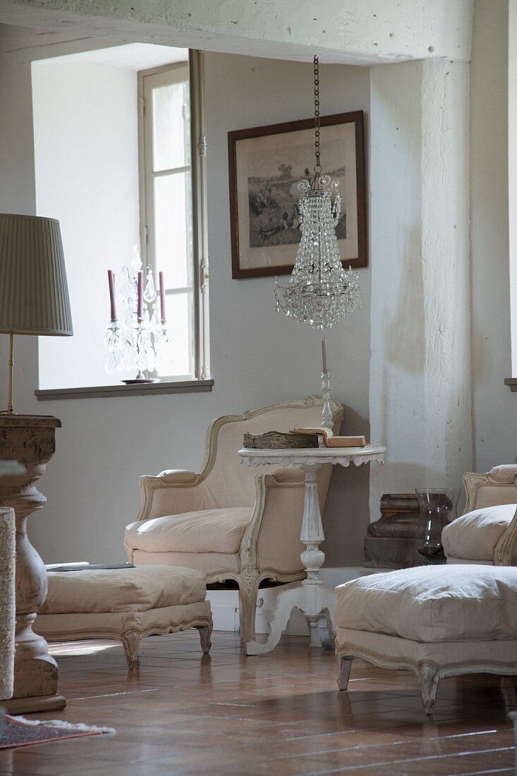 Rococo armchair with pale cover and side table with turned and carved pedestal base below chandelier with glass pendants