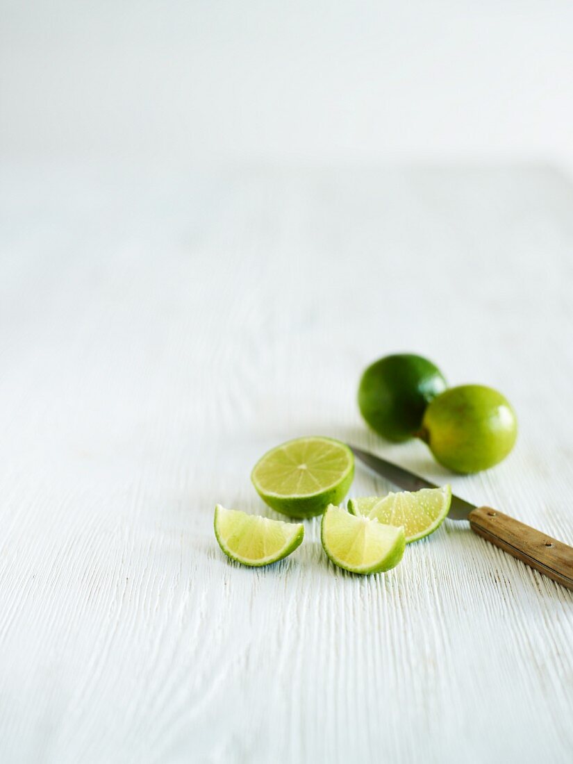 Limes, whole, halved and wedges, with a knife