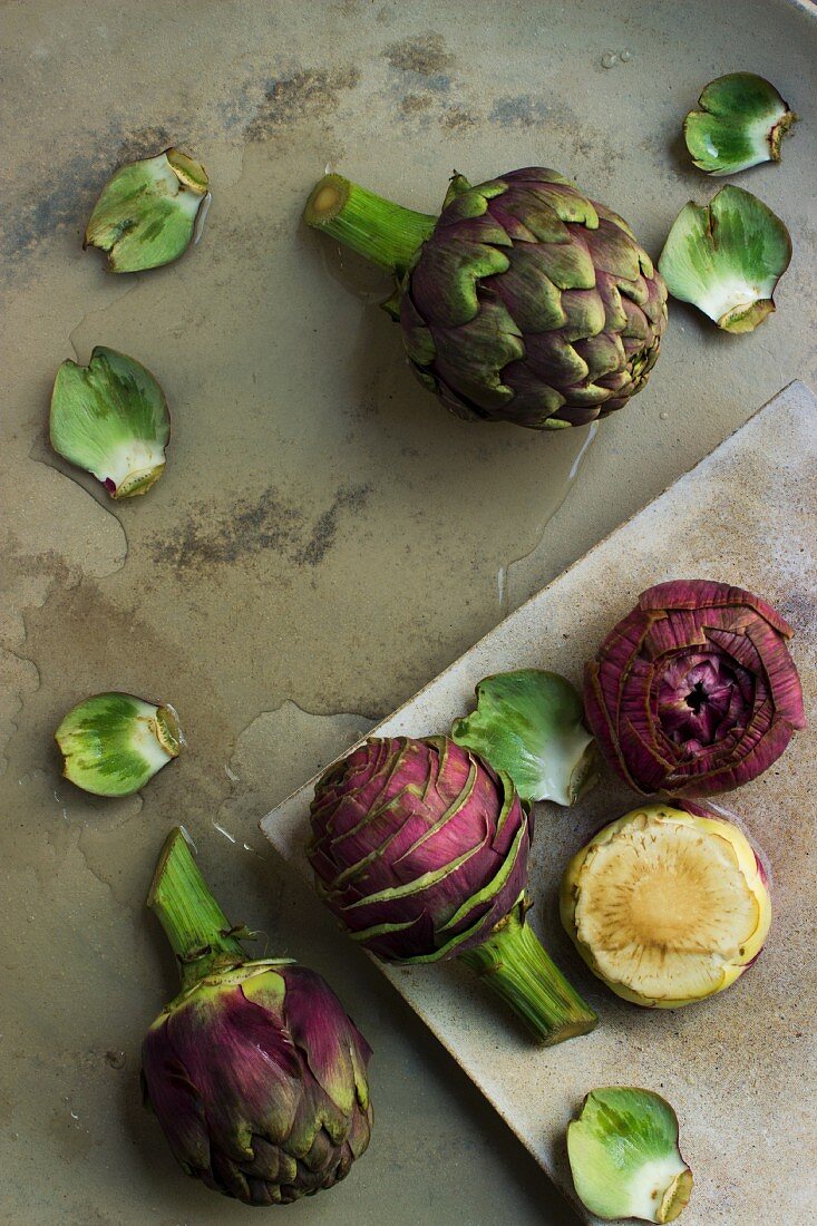 Whole artichokes, prepared artichokes and artichoke hearts on a stone platter