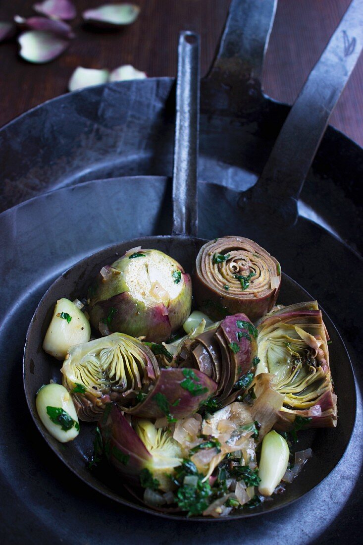 Artichokes with herbs and garlic in a hand-forged iron pan