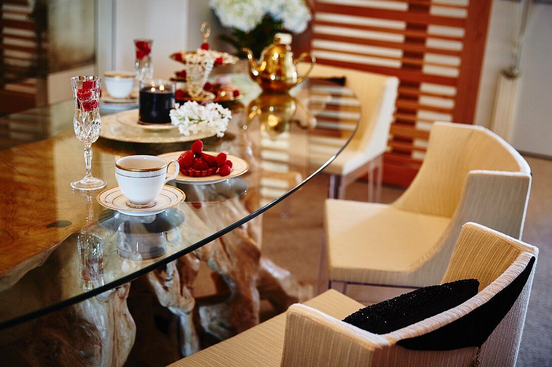 Coffee set, tarts and glasses of Champagne on glass table with upholstered chairs
