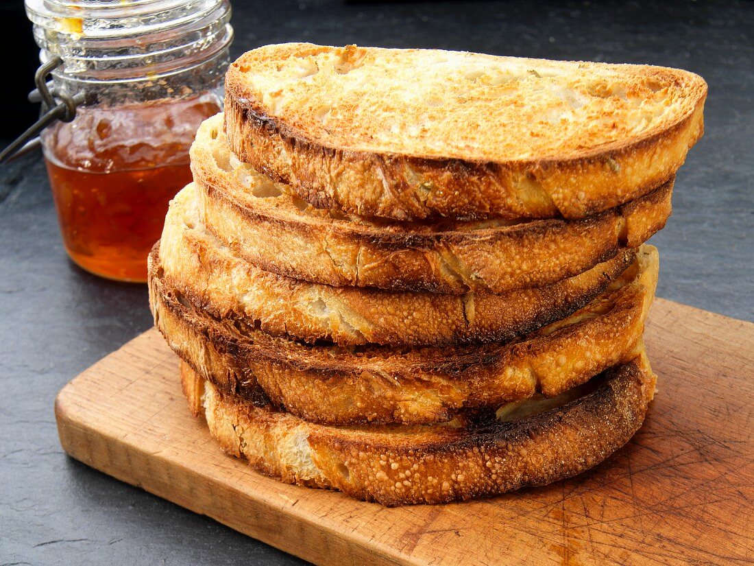 A stack of toast on a chopping board with jam