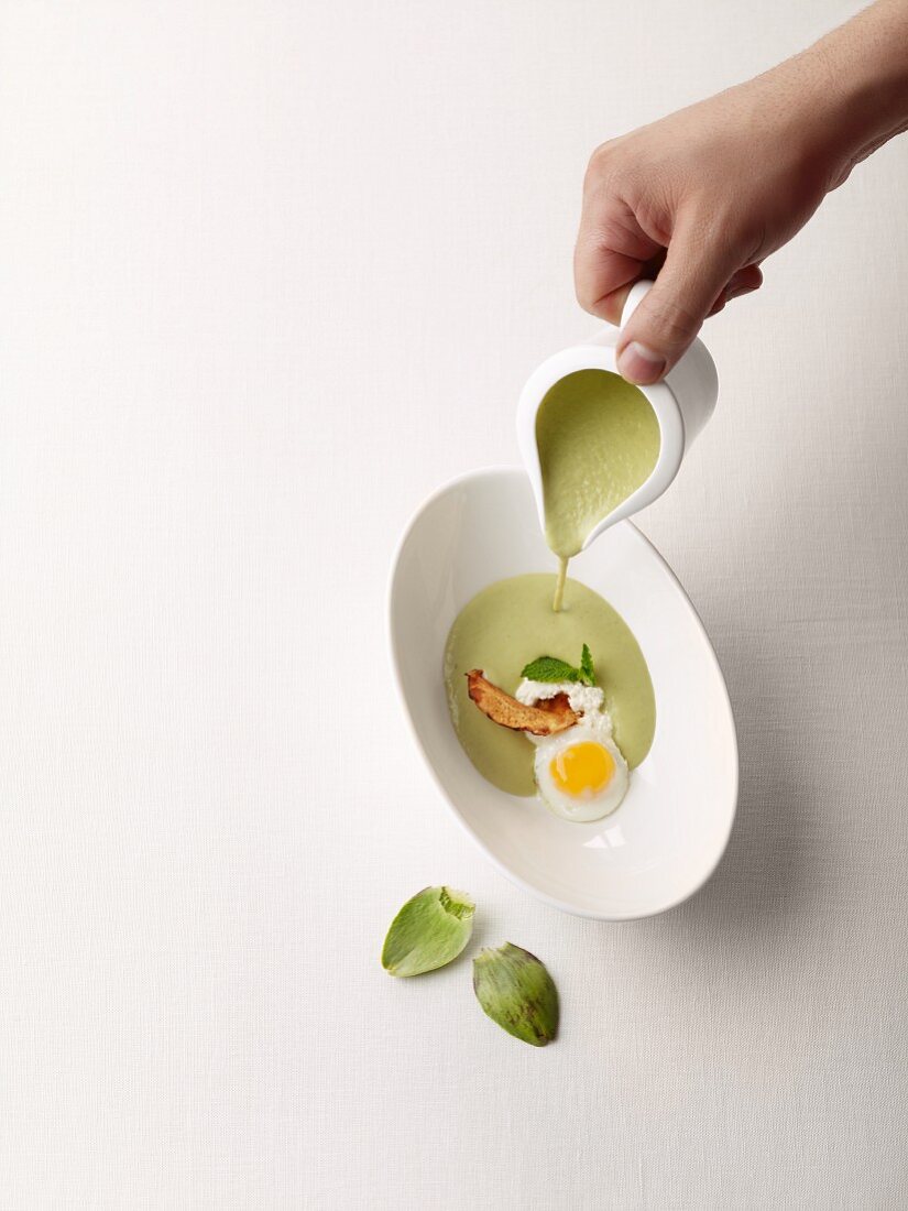 Artichoke soup being poured into a soup plate