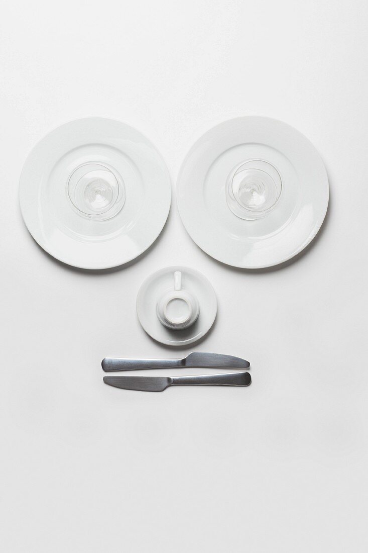 A face made up of plates, glasses, a cup and knives