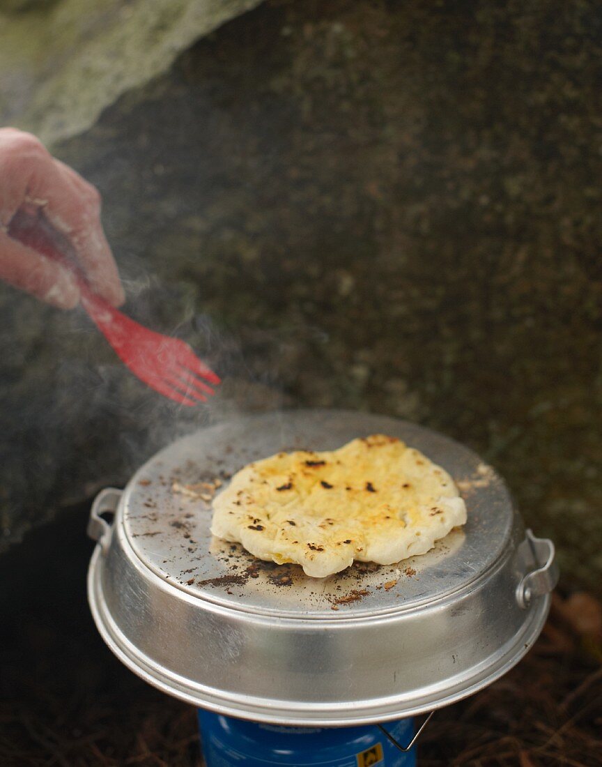 A person baking unleavened bread on a camping cooker