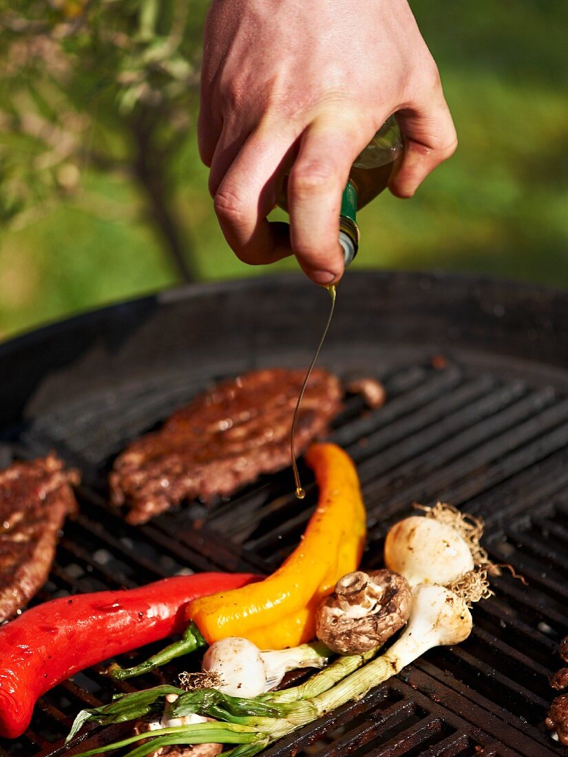 Steak and vegetables on a barbecue being drizzled with olive oil