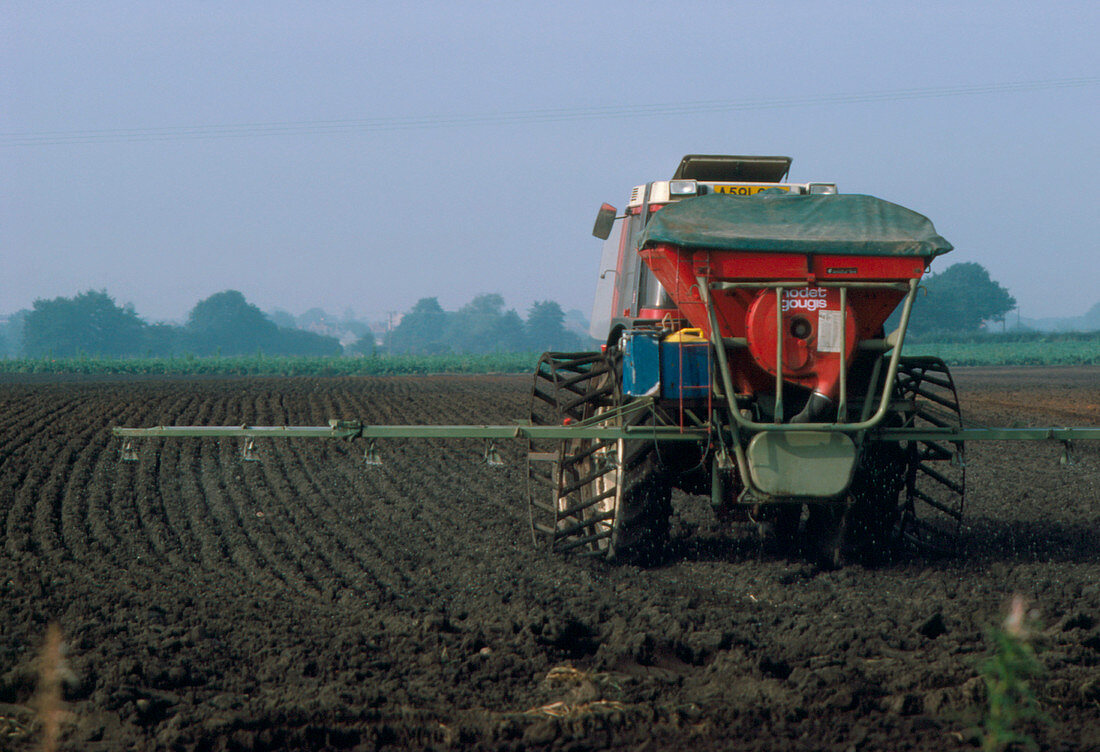 Tractor spreading fertilizer over ploughed land