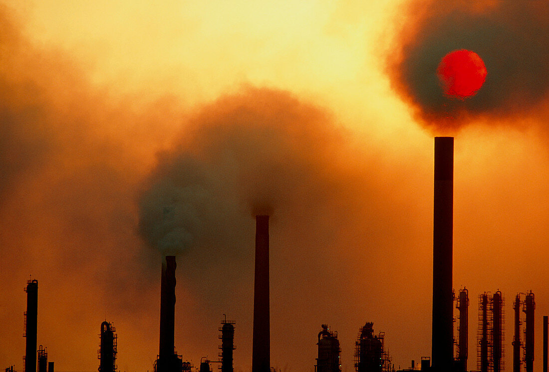 Smoking chimneys of an oil refinery at sunset