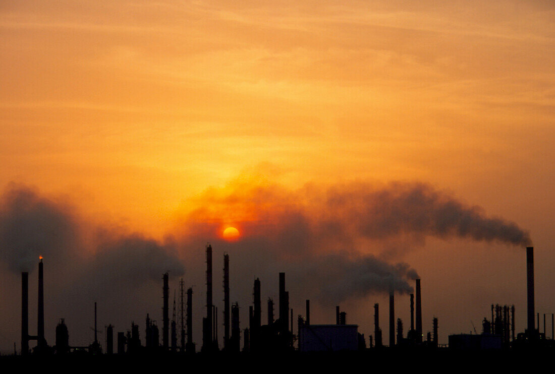 Smoking chimneys of an oil refinery at sunset